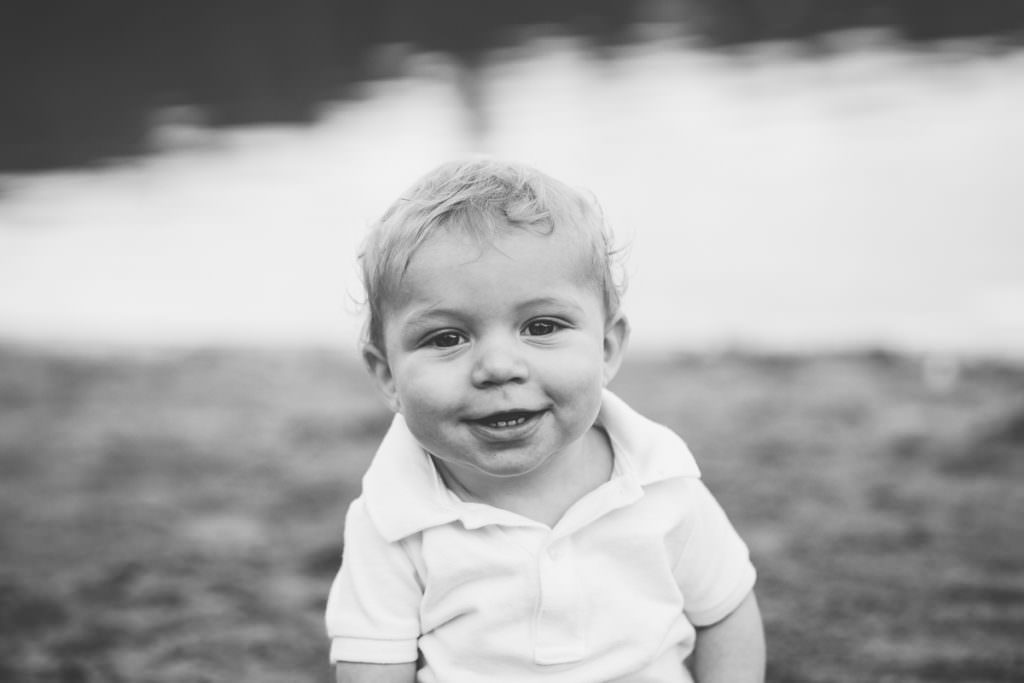 black and white of baby with white shirt sitting in front of lake