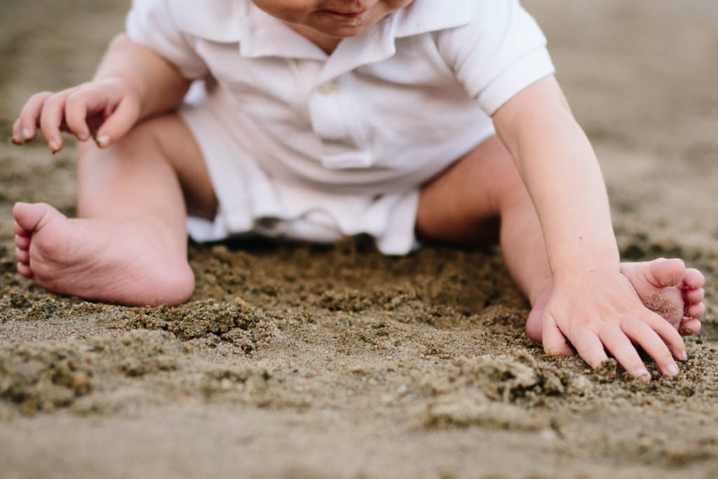 baby boy in white outfit play in the sand at the beach