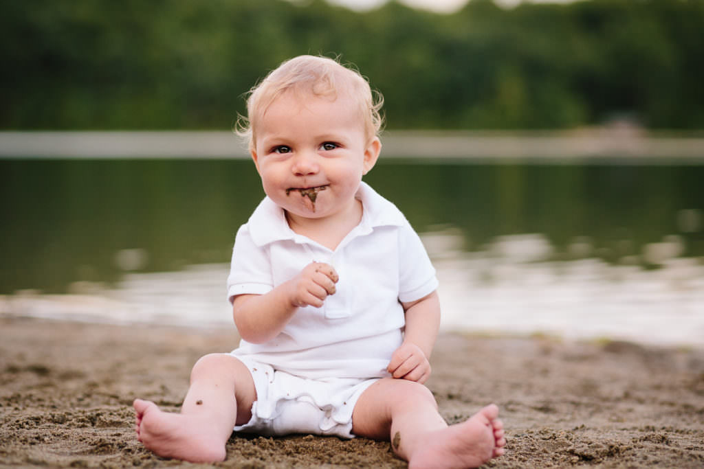 baby boy smiles while drooling out sand he just at a the beach