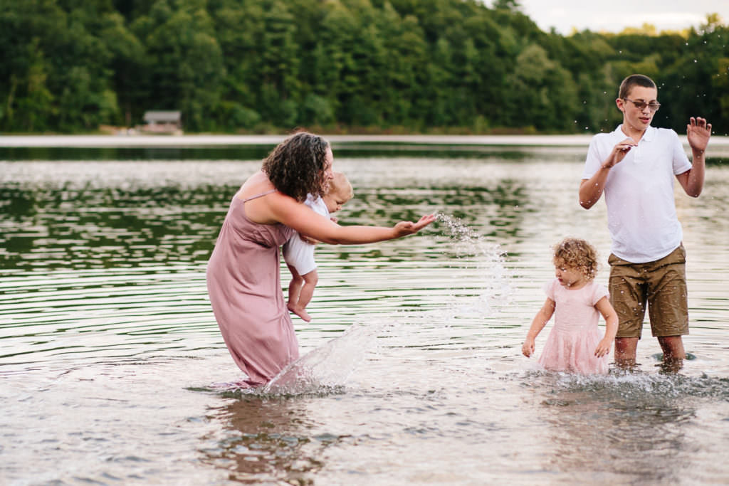 mom holding baby and wearing a long dress playing in the lake