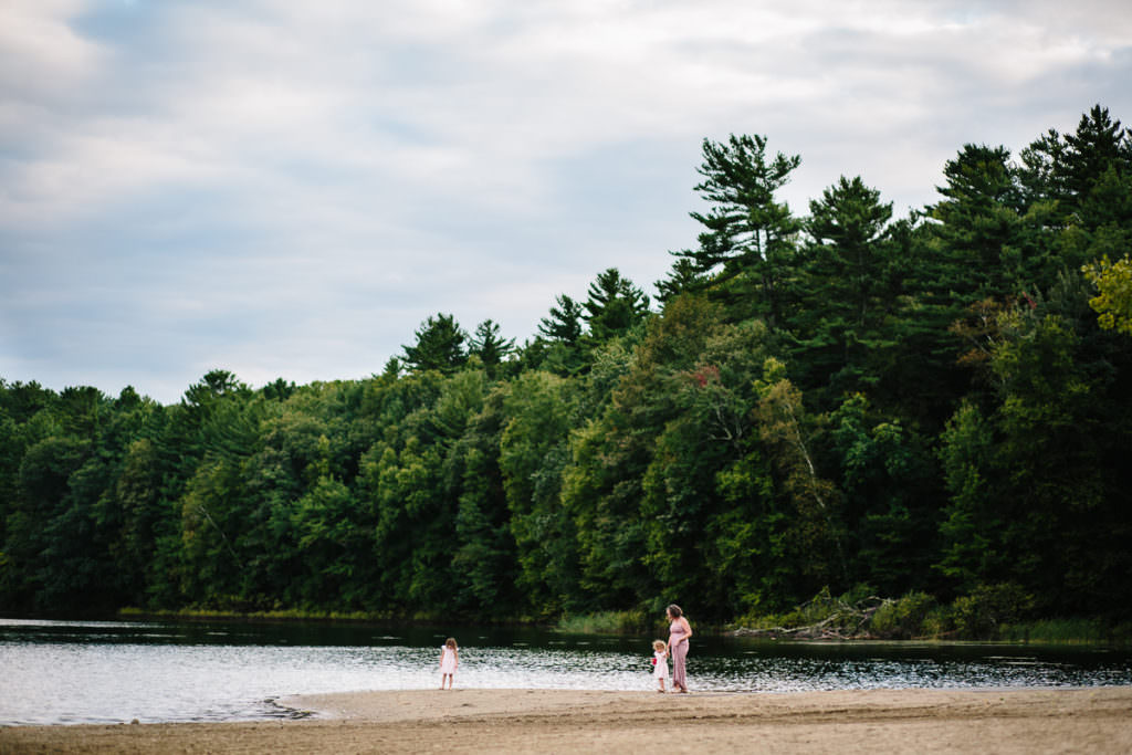 mom and daughters walking on the beach with green trees and sand