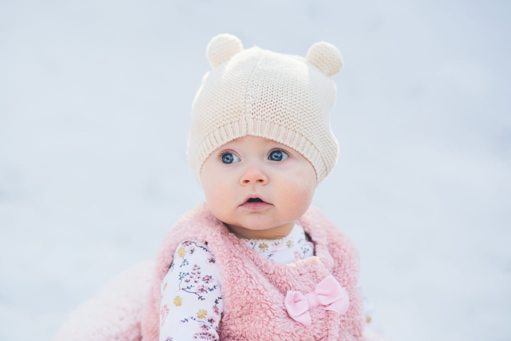 Saratoga Springs New York photographer baby sitting in snow with fuzzy hat