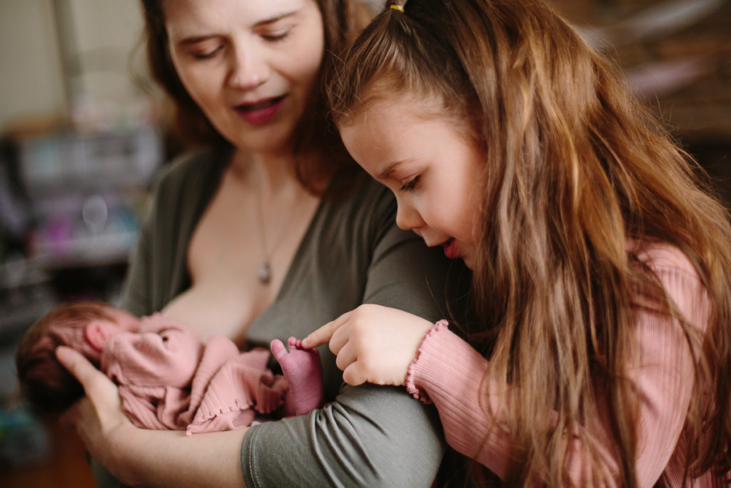 sister checking out baby sister breastfeeding