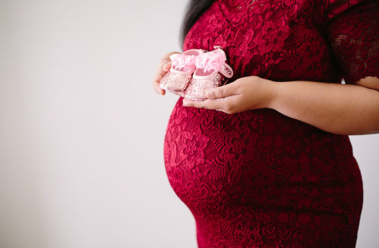 mom holding baby shoes next to pregnant belly