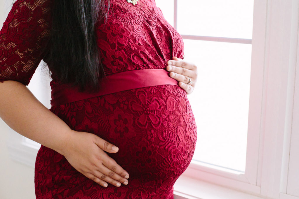 mom holding pregnant belly in red dress