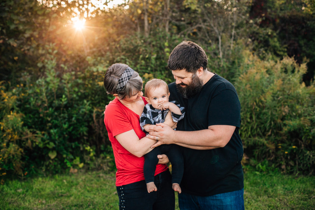 mom and dad holding baby with sun shine behind them