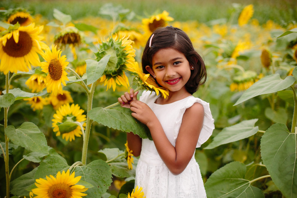little girl in white dress holding a sunflower